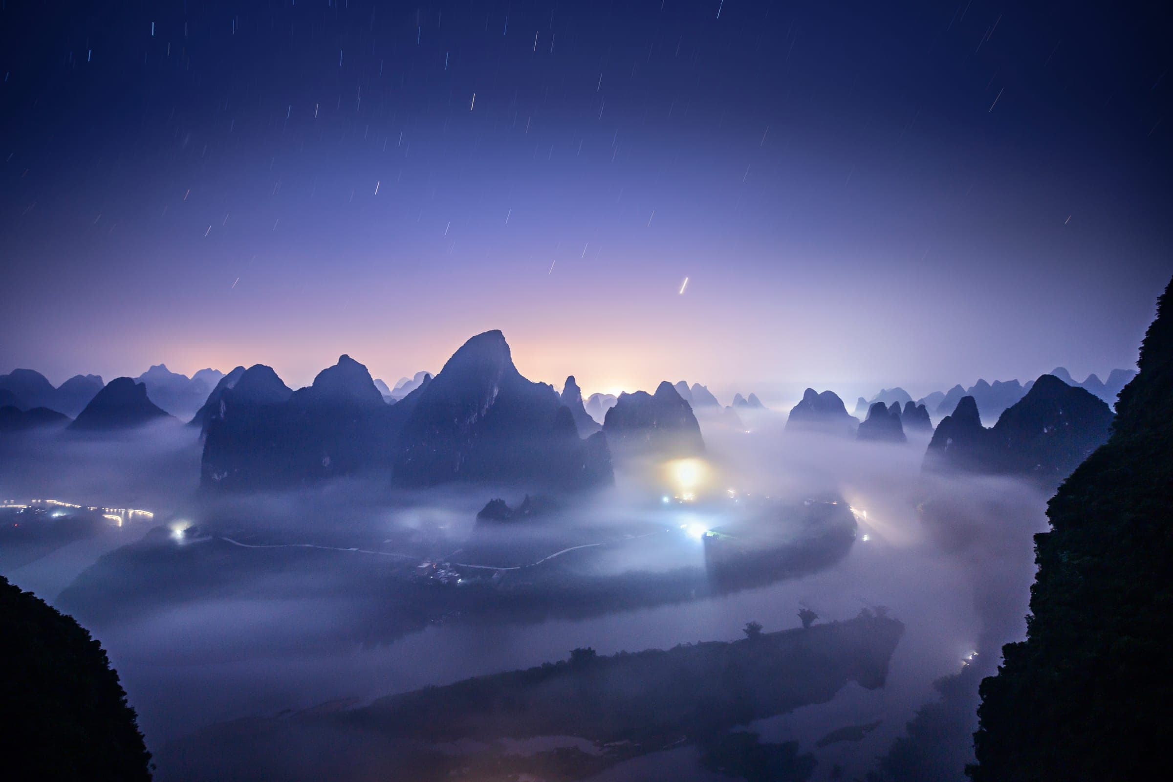 A valley under a night sky, its river in fog
